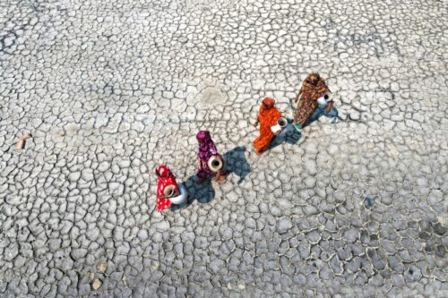 Vier vrouwen lopen over uitgedroogde grond om water te halen