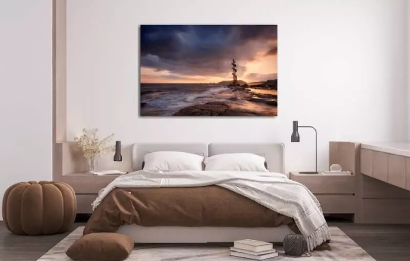 Slaapkamer met foto op plexiglas boven bed met daarop een vuurtoren bij zonsondergang